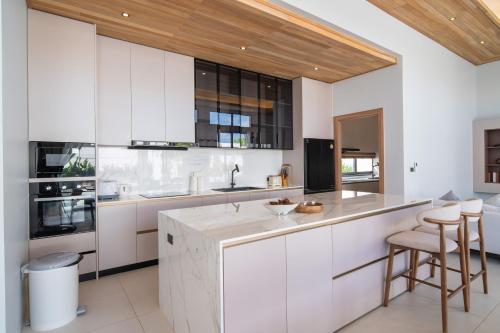 a kitchen with white cabinets and a counter with stools at Mouana Breeze Mai Khao VIP 4-bedroom Pool Villa 9911 in Phuket