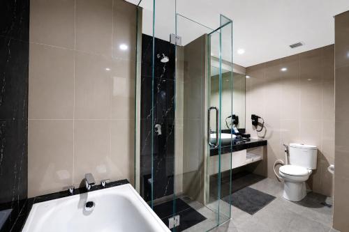 a bathroom with a tub and a toilet and a glass shower at StarRay Hotel Jakarta Kebayoran in Jakarta