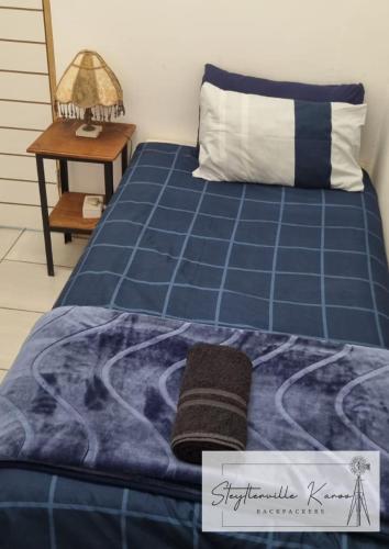 a bed with a blue comforter and a table at Steytlerville Karoo Backpackers in Steytlerville