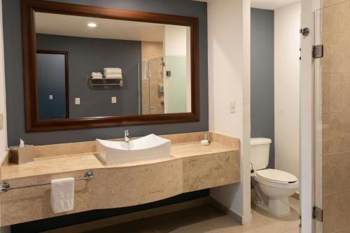 a bathroom with a sink and a toilet and a mirror at Courtyard by Marriott Guadalajara Andares in Zapopan