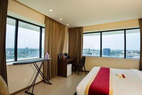 a hotel room with a bed and a desk and windows at Ascot Hotel in Kozhikode