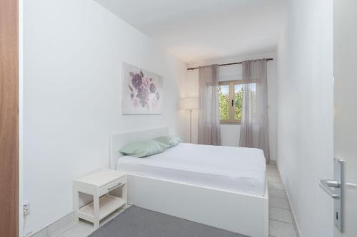 a white bedroom with a bed and a window at Apartments Zeljko in Pag