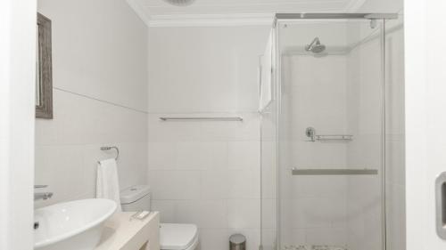 a white bathroom with a shower and a sink at Stonehouse on Main in Struisbaai