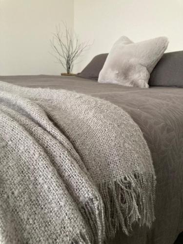 a bed with a gray blanket and pillows on it at The Batch in Oamaru