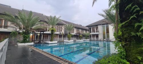 a large swimming pool with palm trees in front of a building at CaiPods Backpacker Hostel by G10 Guest House Bandung in Bandung