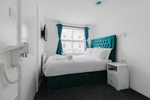 a bedroom with a bed with a blue headboard and a window at Whiteleys Hotel in London