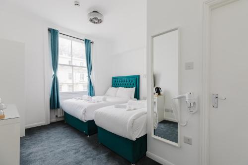 two beds in a white room with a mirror at Whiteleys Hotel in London
