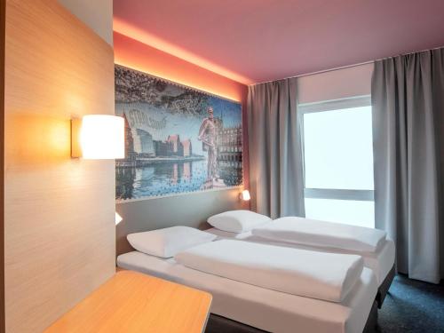 three beds in a room with a painting on the wall at B&B HOTEL Stralsund in Stralsund