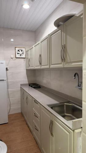 a kitchen with white cabinets and a sink and a refrigerator at ريف سويت للشقق المخدومة in Al Namas