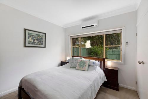 a white bedroom with a bed and a window at Family stay minute walk from Hargraves beach in Norah