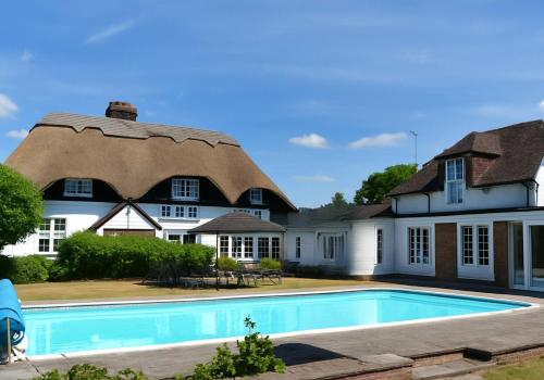 a house with a thatched roof and a swimming pool at Beautiful Thatched Cottage with Outdoor Pool, Secure Garden, Dog & Family Friendly! Chichester Holiday Properties in Bosham