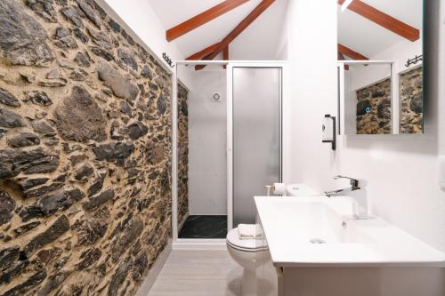 a bathroom with a stone wall and a toilet and sink at Seixal Sunny Villa A & B by Amazing Madeira in Seixal