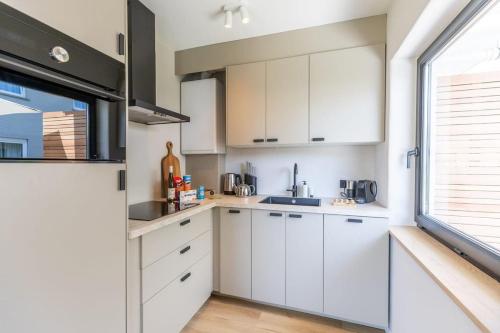 a kitchen with white cabinets and a window at Casiola - Charming Apartment with Garden & Parking in Cadzand