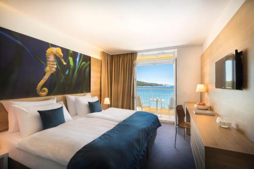 a hotel room with a bed and a desk and a window at Remisens Hotel Epidaurus-All inclusive in Cavtat