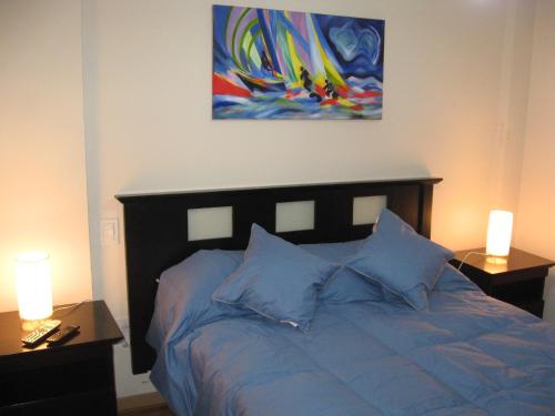 a bedroom with a bed with blue pillows and a painting at Bahiaxdia Paraguay in Bahía Blanca