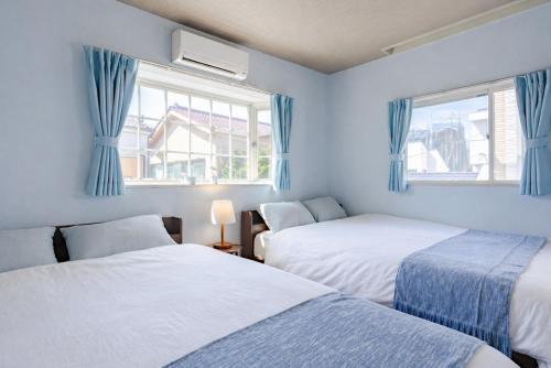 two beds in a room with blue curtains and windows at 75m2 10people private house rental 8beds 8min Ikebukuro 13min Shinjuku 18min Shibuya Englishspeaking staff available in Tokyo