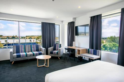 ein Hotelzimmer mit einem Bett und Stühlen sowie einem Schreibtisch in der Unterkunft Alpha Hotel Eastern Creek in Blacktown