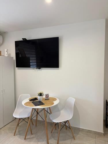 a table with white chairs and a tv on a wall at Apartman Diamond LUX in Surčin