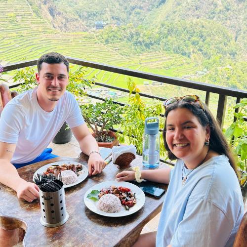 a man and a woman sitting at a table with food at Batad Pension and Restaurant Native House in Banaue