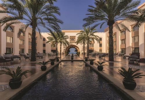 a courtyard with palm trees and a pool in a building at Al Husn Hotel Muscat - managed by Hilton in Muscat