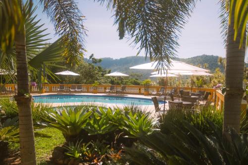 a swimming pool with tables and chairs and umbrellas at Pousada Vale do Dinossauro in São Pedro