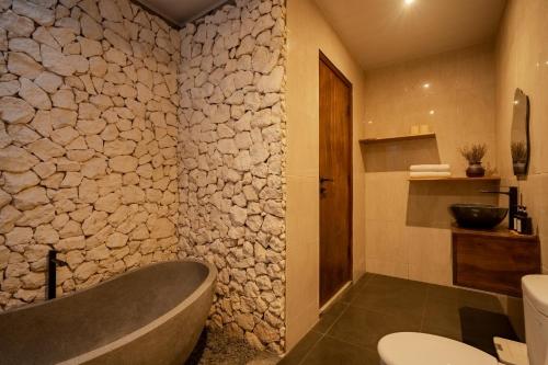 a bathroom with a bath tub and a stone wall at Maheeka Villa, Sanur in Sanur