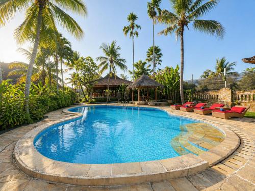 a swimming pool with chairs and palm trees at Saren Indah Hotel in Ubud