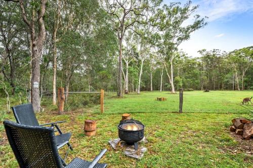 a fire pit with two chairs and a grill in a field at Clarence Farm Stay by Tiny Away in Maclean