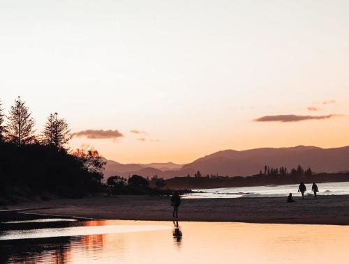 a group of people walking on the beach at sunset at Hinterland Hideout by Tiny Away in Myocum