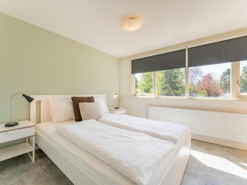 a white bedroom with a large bed and windows at Kuifmees in Hulshorst