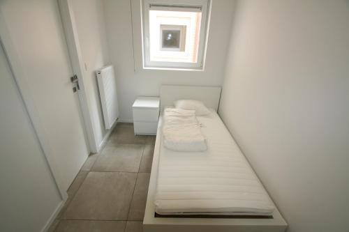 um pequeno quarto branco com uma cama e uma janela em Dolce Vita Nieuwpoort em Nieuwpoort