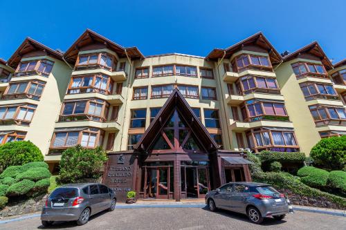 two cars parked in front of a large building at Flat Serrano com Total Acesso ao Wish Resort in Gramado