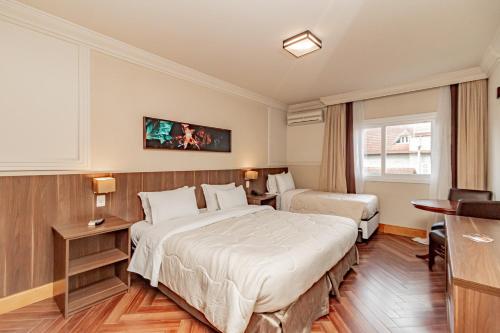 a hotel room with two beds and a desk at Flat Serrano com Total Acesso ao Wish Resort in Gramado