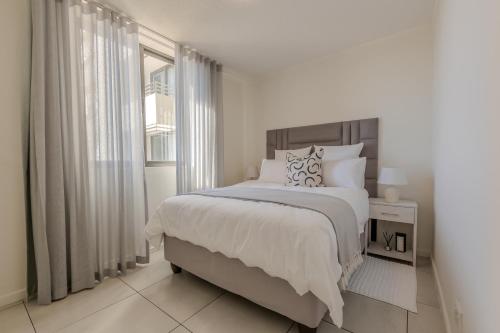 a white bedroom with a large bed and a window at The Stay Edit Windhoek in Windhoek