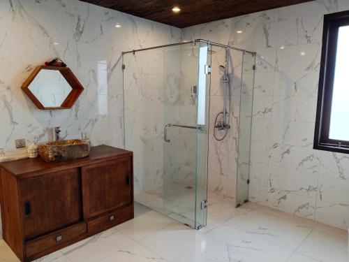 a glass shower in a bathroom with a wooden cabinet at Merlyn Meadows Retreat in Munduk