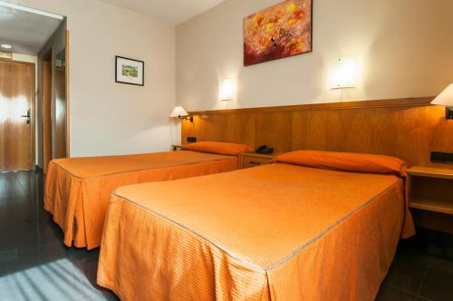 two beds in a hotel room with orange sheets at Hotel Ruta de Europa in Vitoria-Gasteiz