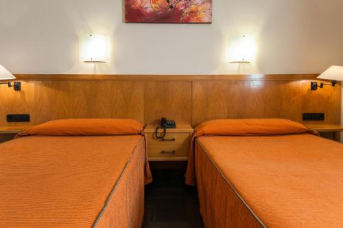 two beds in a room with two lamps on the wall at Hotel Ruta de Europa in Vitoria-Gasteiz