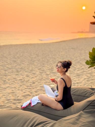a woman sitting on a blanket on the beach with a laptop at Serendipity Mirissa in Mirissa