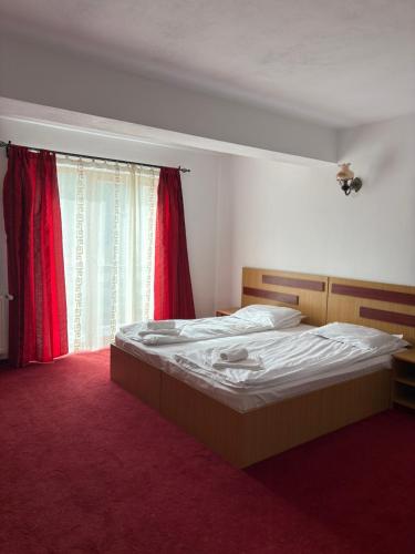 a bedroom with a bed and a window with red curtains at Vila dintre Brazi in Moieciu de Jos