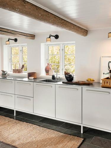 a white kitchen with white cabinets and windows at Historic Vipp House From 1775 In Søllested in Søllested