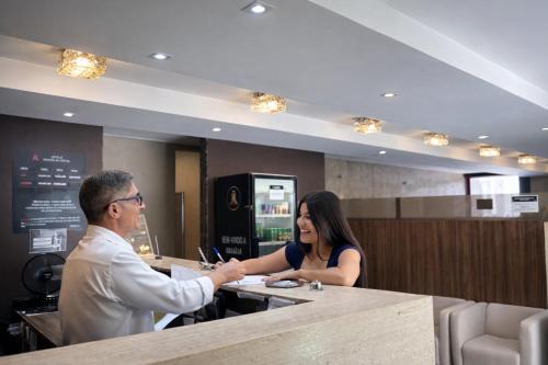 a man shaking hands with a woman at a counter at Athus Brasilia Hotel by Bsb Inn in Brasília