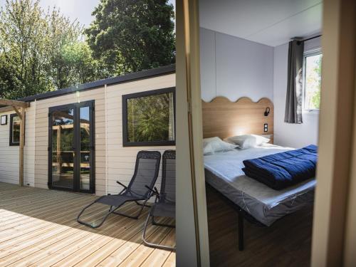a bedroom on a deck with a bed and a chair at Camping Terre d'Armor in Bourseul