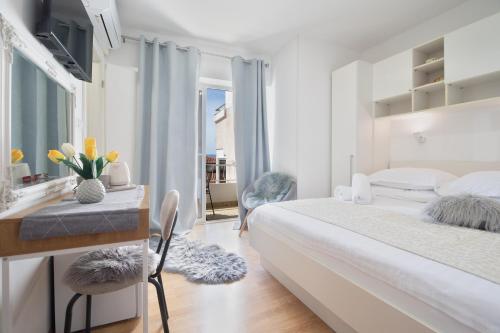 a white bedroom with a bed and a desk with flowers at Apartment & Rooms Meri Tučepi in Tučepi