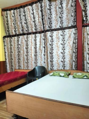 a room with two beds and a chair in front of a curtain at Oasis Lodge in Jorhat
