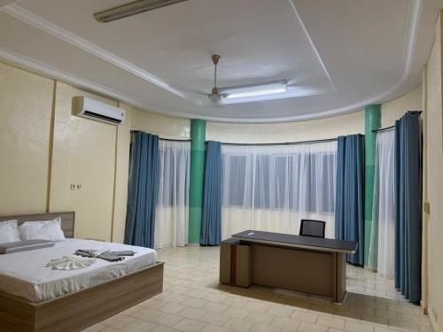 a bedroom with a bed and a desk and curtains at Lilia Business Hotel in Ouagadougou