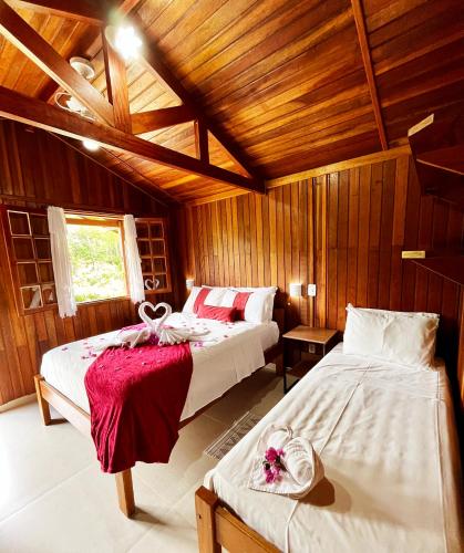 two beds in a room with wooden walls at Pousada da Cachoeira in Monte Alegre do Sul