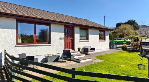 a white house with a red door and some chairs at The Hirsel on Skye in Ord