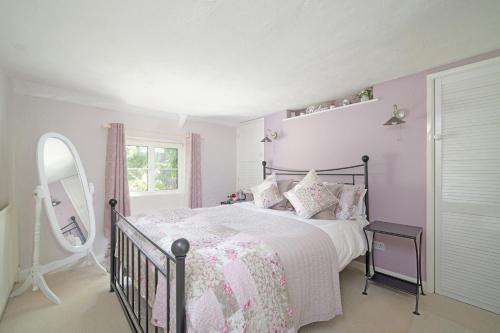 a pink and white bedroom with a bed and a mirror at Lavender Cottage in Gillingham
