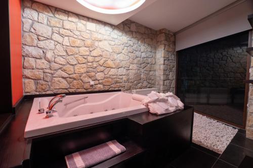 a bathroom with a tub and a stone wall at Nymfes Hotel in Kato Loutraki