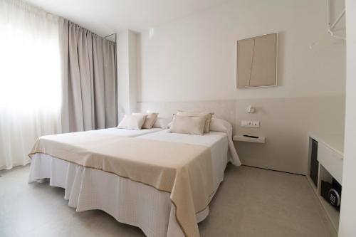 a white bedroom with two beds and a cabinet at Hotel Roca Plana in L'Ampolla